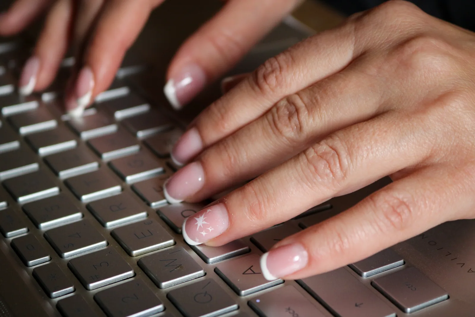 Finom, világos francia manikűrös kéz gépel a laptop billentyűzetén