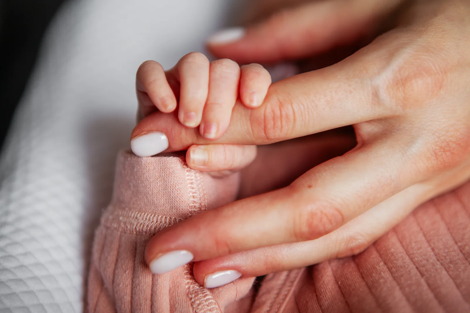 Csecsemő keze egy felnőtt ujját fogja, a felnőtt körmei tejesfehérek és ápoltak